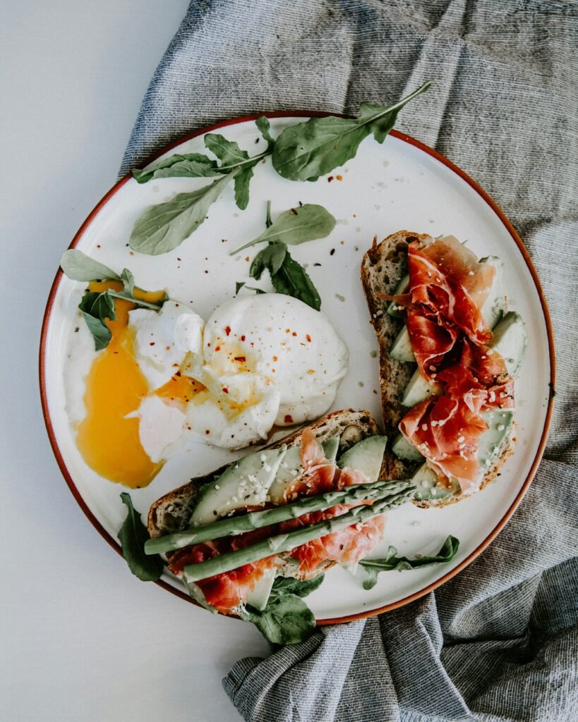 A top view of an appetizing meal in a plate composed of bruschetta, egg, a mozzarella ball, and some asparagus.
