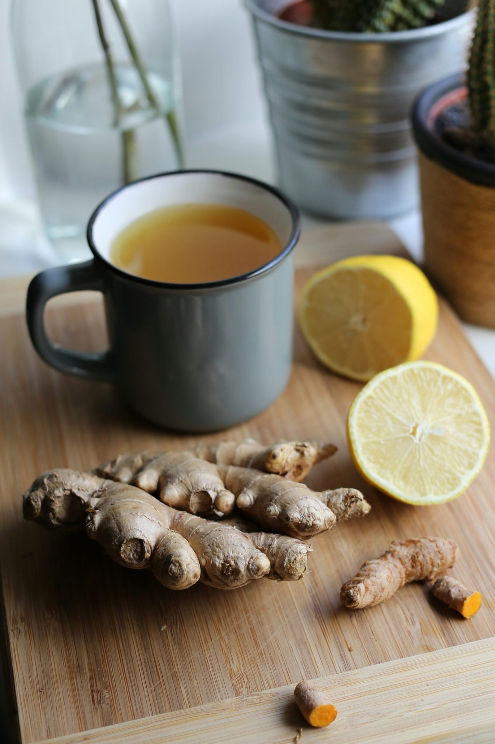 A cup of ginger lemon tea on a wooden chopping board with fresh ginger and a sliced lemon