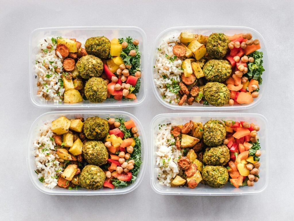 A meal planning sample is displayed from above. There are 4 containers filled with the same meal: rice, roasted vegetables, meatballs, and a chickpea salad.