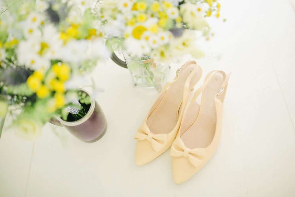A pair of cute yellow heels is displayed next to flower vases