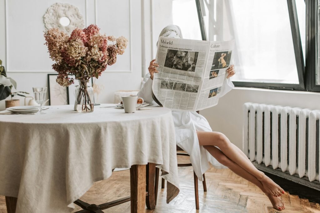 Woman enjoying a relaxing morning in mess-free home reading a newspaper with coffee in a cozy setting.